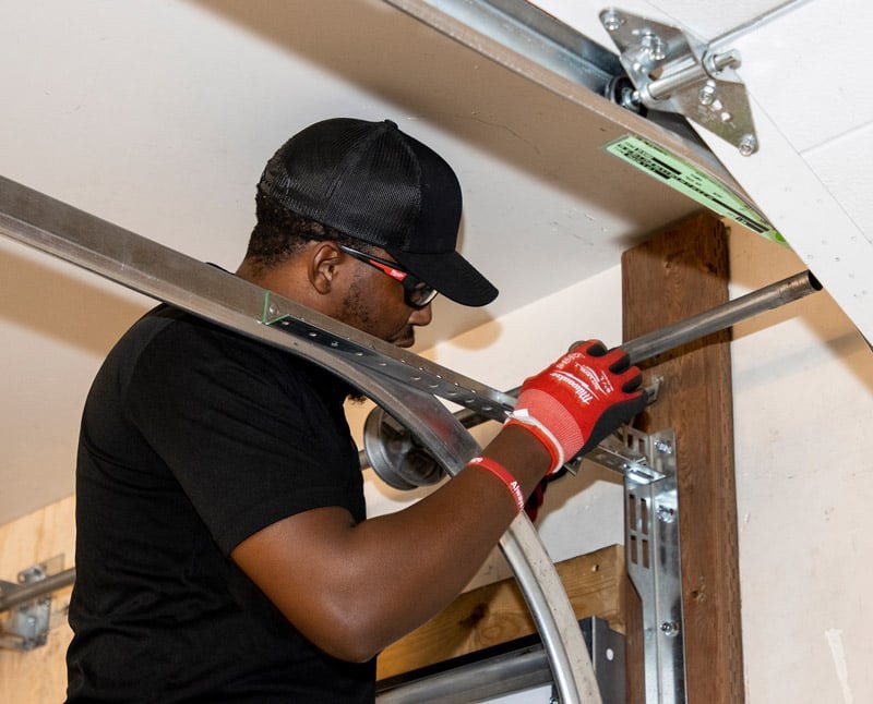 An A1 technician in a black shirt and red gloves working on the spring and track of an open garage door