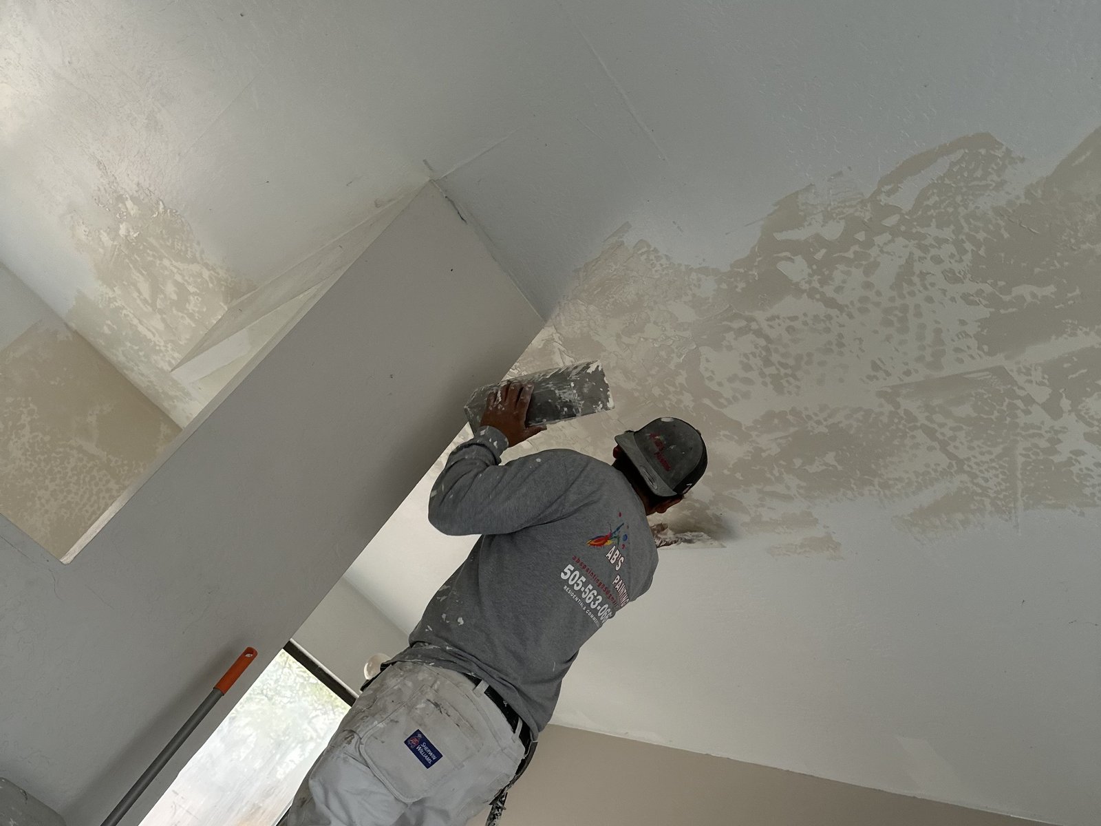 A worker in an AB's Painting shirt spreading drywall compound over a patched ceiling
