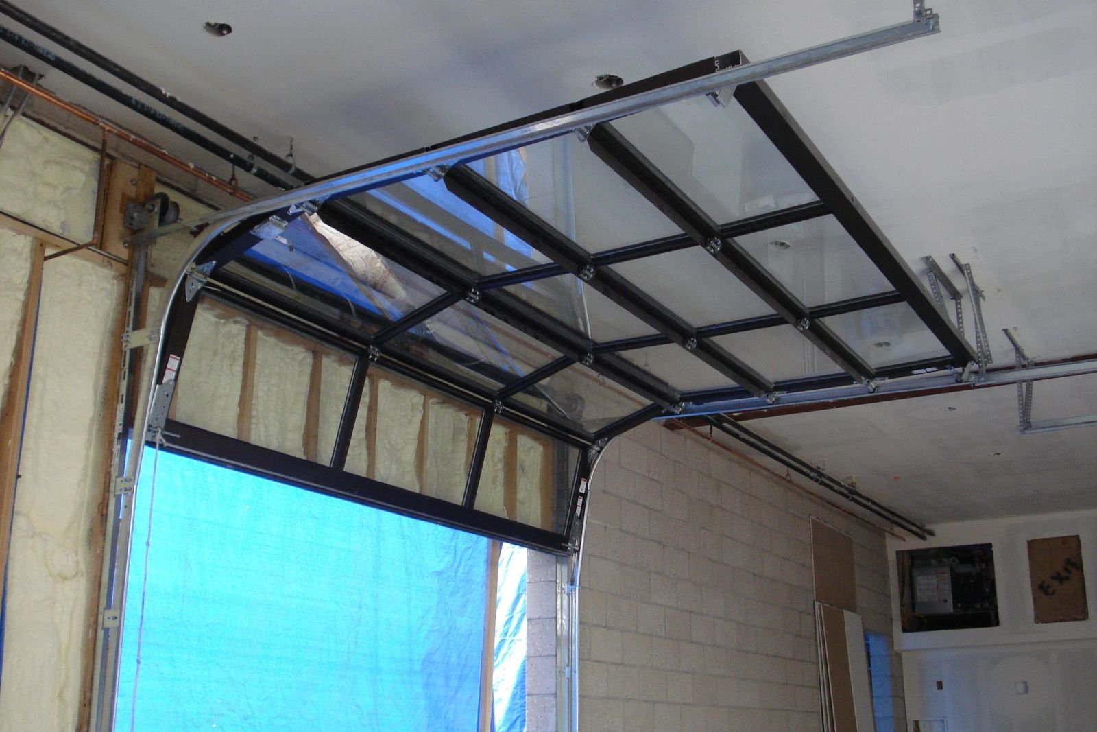 A glass-paneled garage door raised on high-lift track inside an unfinished garage