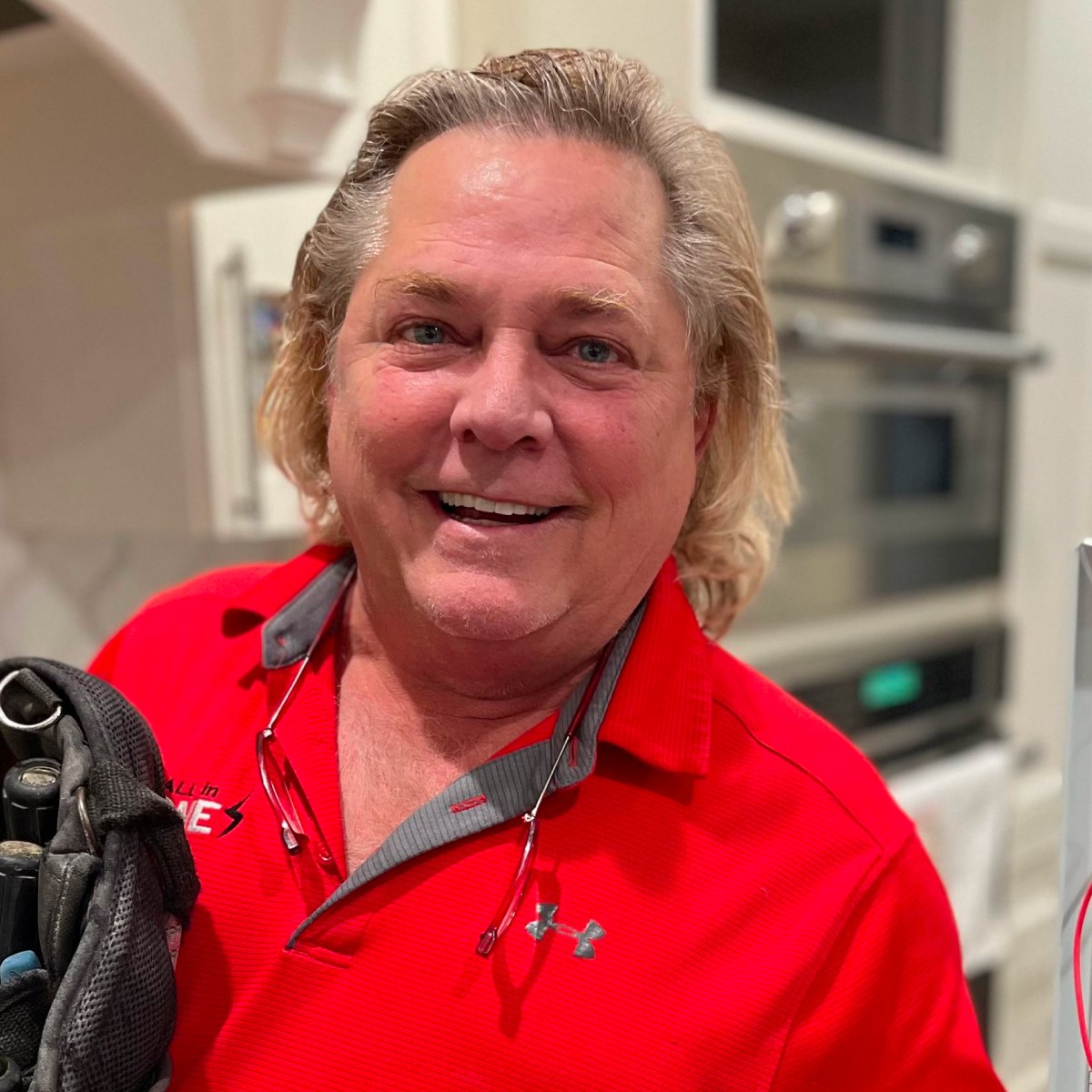 Smiling electrician in red All In One Electric shirt holding a tool bag