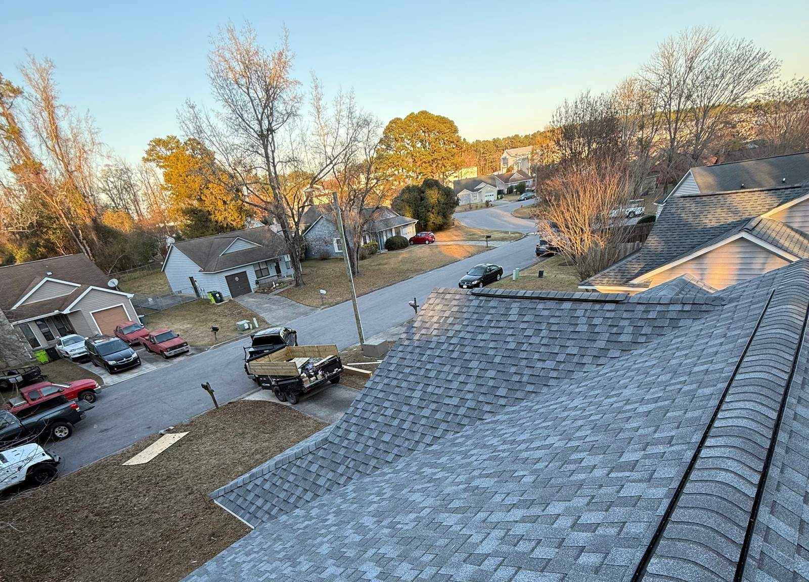New gray architectural shingles on a sloped roof, with a residential street, parked cars and a loaded trailer below