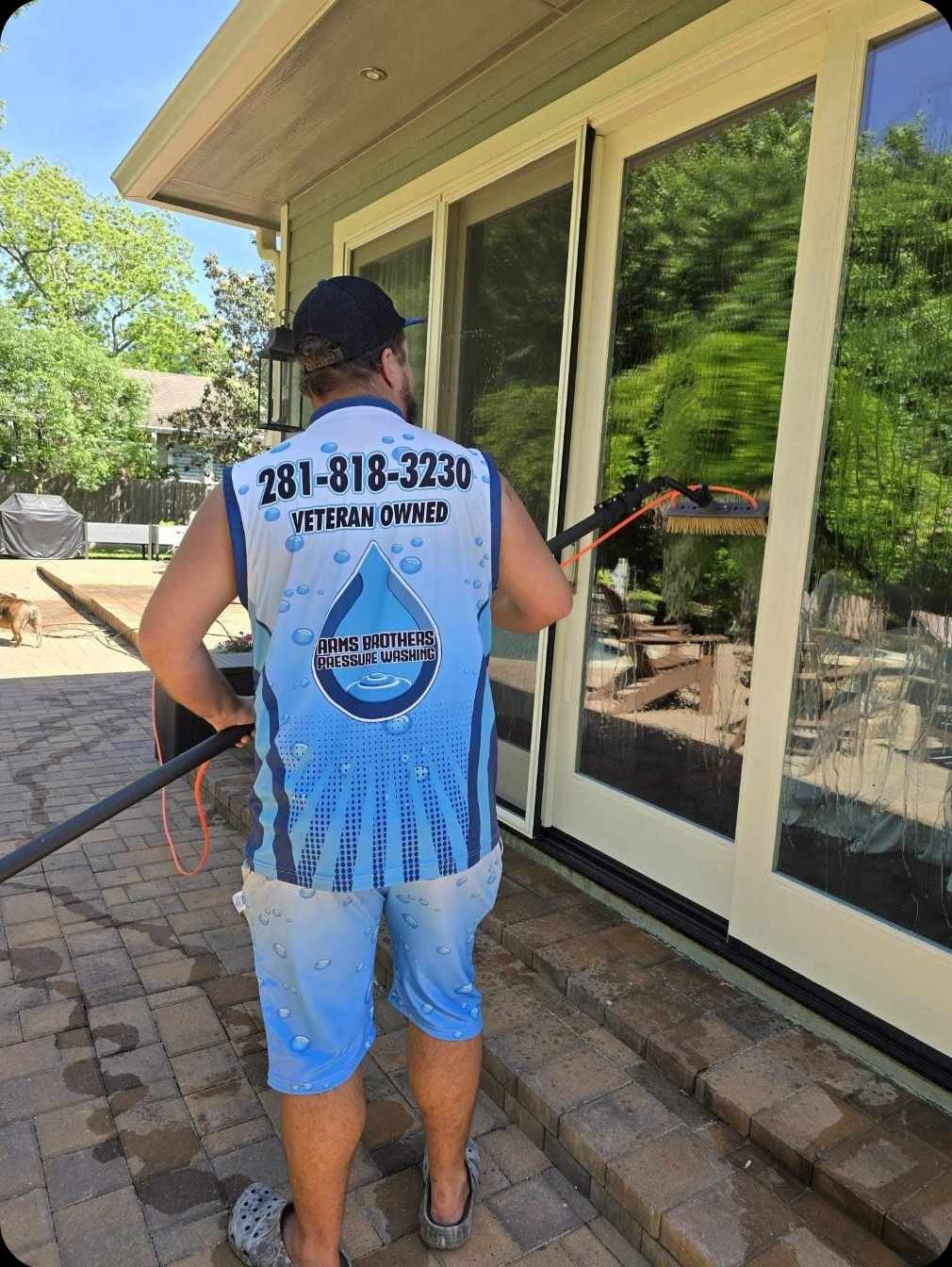 Worker in an Arms Brothers Pressure Washing veteran-owned vest cleaning glass patio doors with a long-handled brush on a brick paver patio