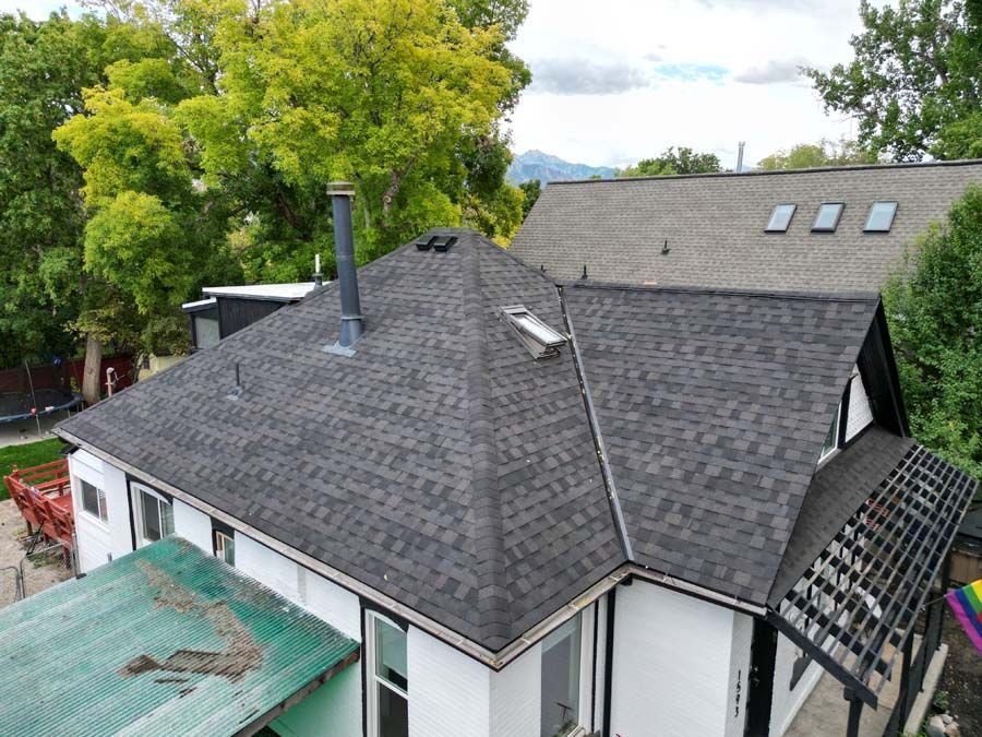 Aerial view of a house with a new dark shingle hip roof, a skylight and a metal chimney pipe.