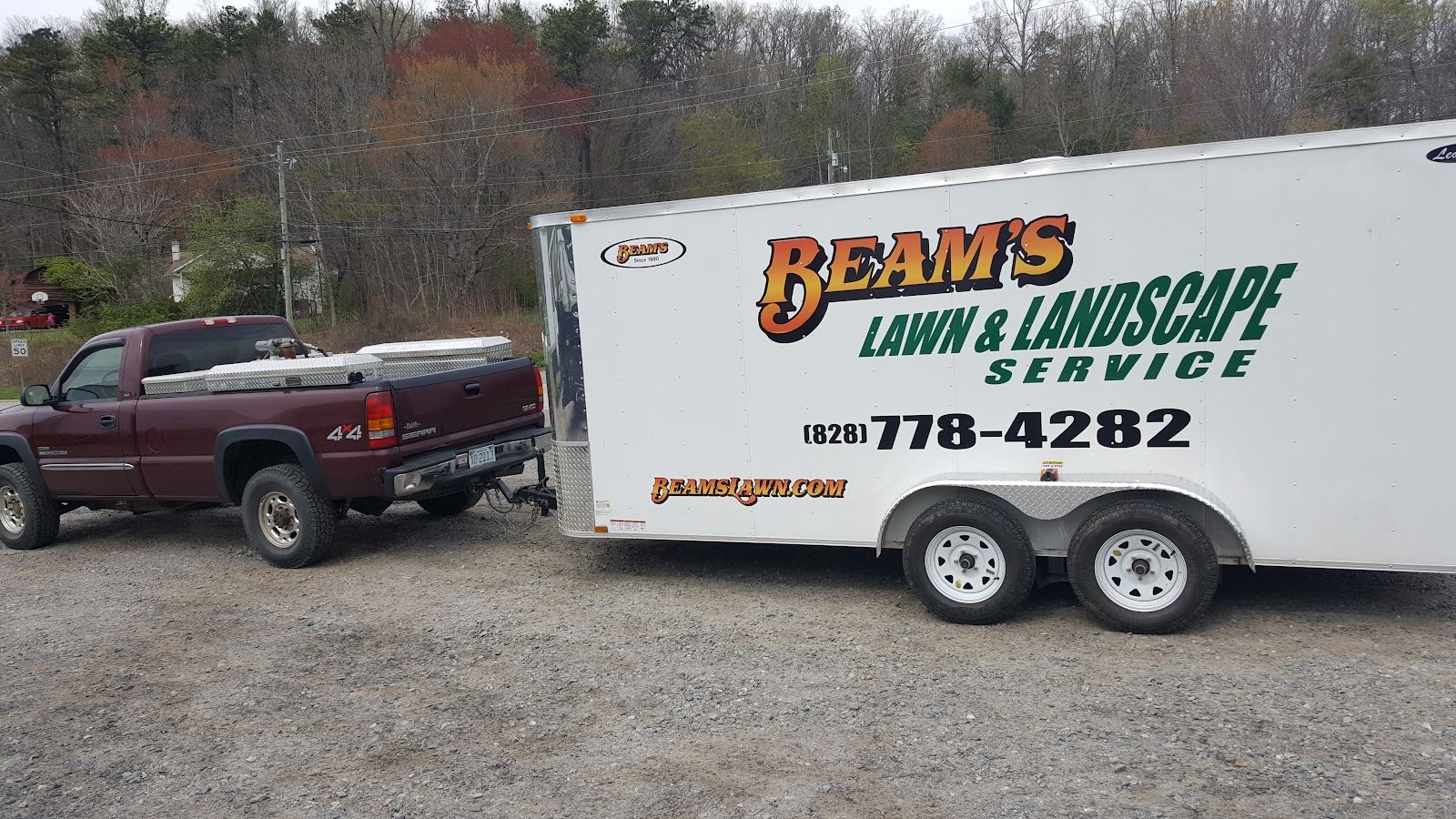 A maroon pickup towing a white enclosed trailer lettered Beam's Lawn & Landscape Service, parked on a gravel lot