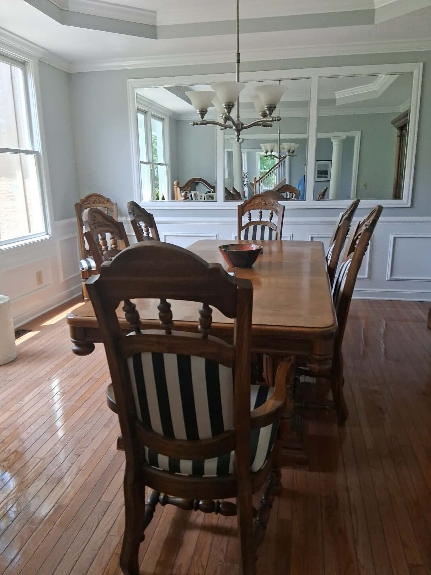 Dining room with a wooden table and striped-cushion chairs, polished hardwood floor, and a large wall mirror