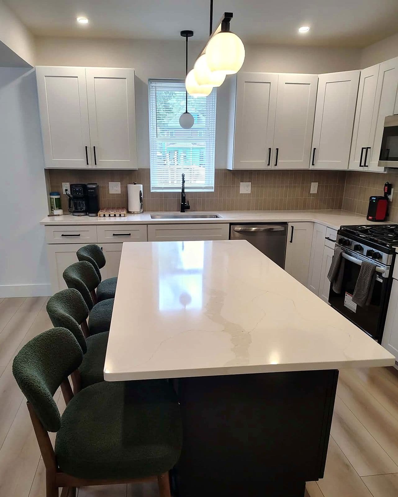 Bright kitchen with white cabinets, a large quartz island, green stools, and a gas range
