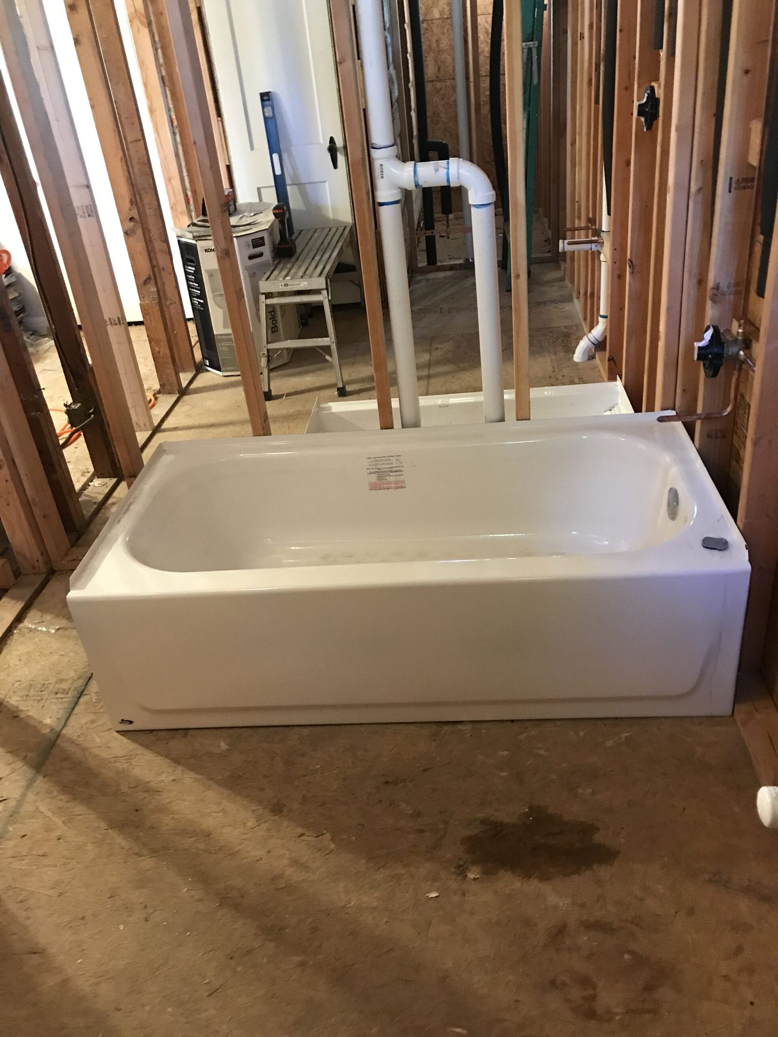 New white bathtub set in a framed-out wall with white PVC drain and vent pipes rising behind it