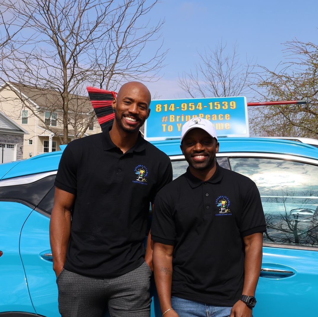 Two Cadabra Cleaning team members in branded polos beside the company car