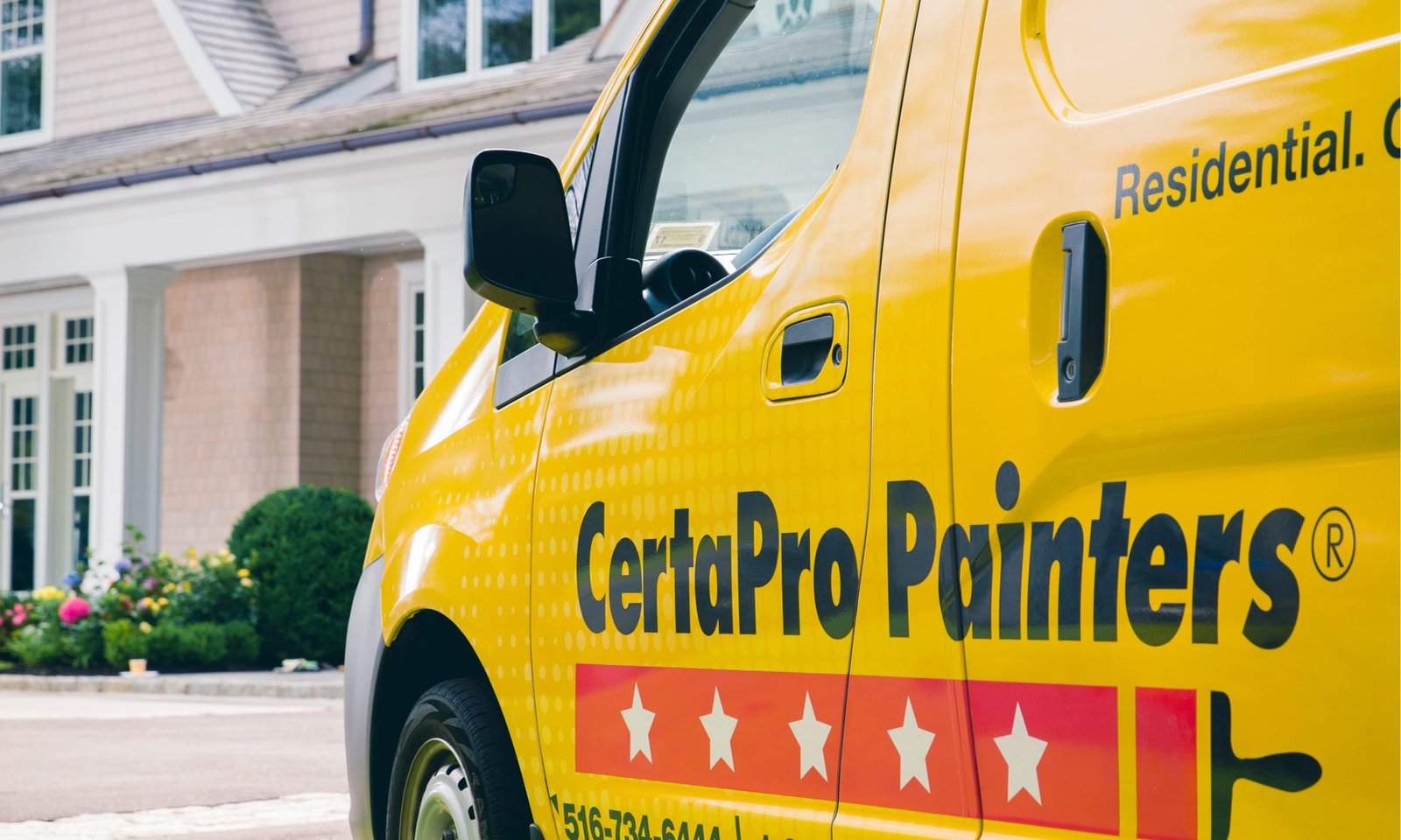 Yellow CertaPro Painters van parked in front of a shingled house with landscaped shrubs and flowers