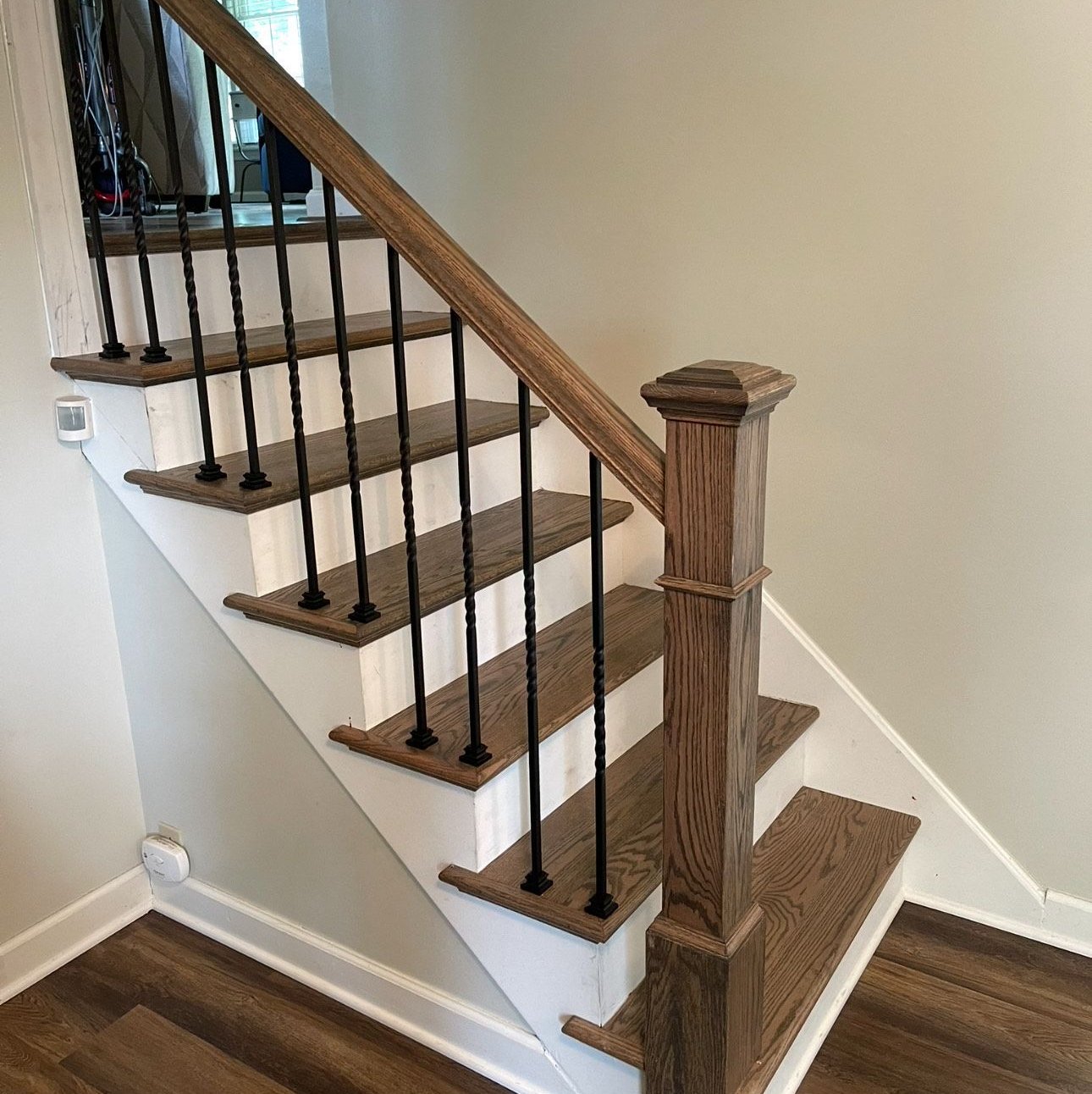 A staircase with brown treads, white risers, a wooden handrail and newel post, and black twisted spindles, above a plank floor