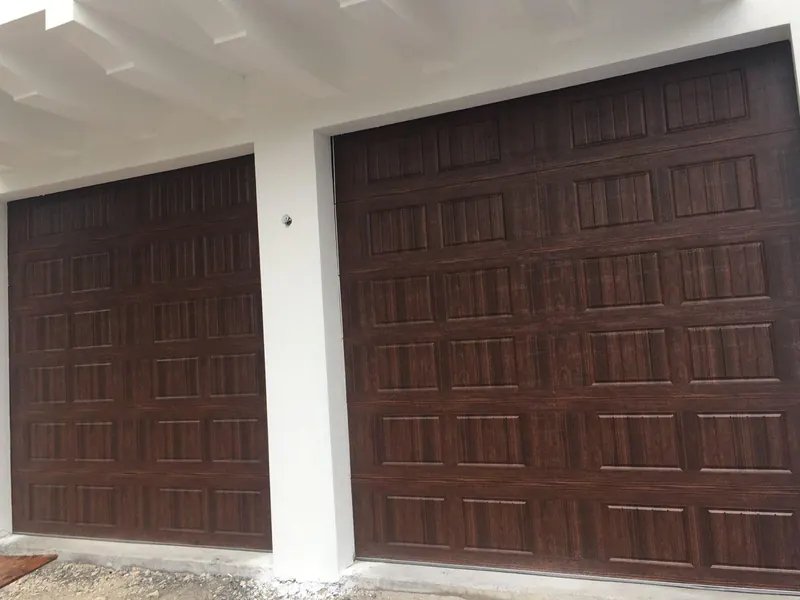 Two dark wood-grain paneled garage doors set in a white stucco wall