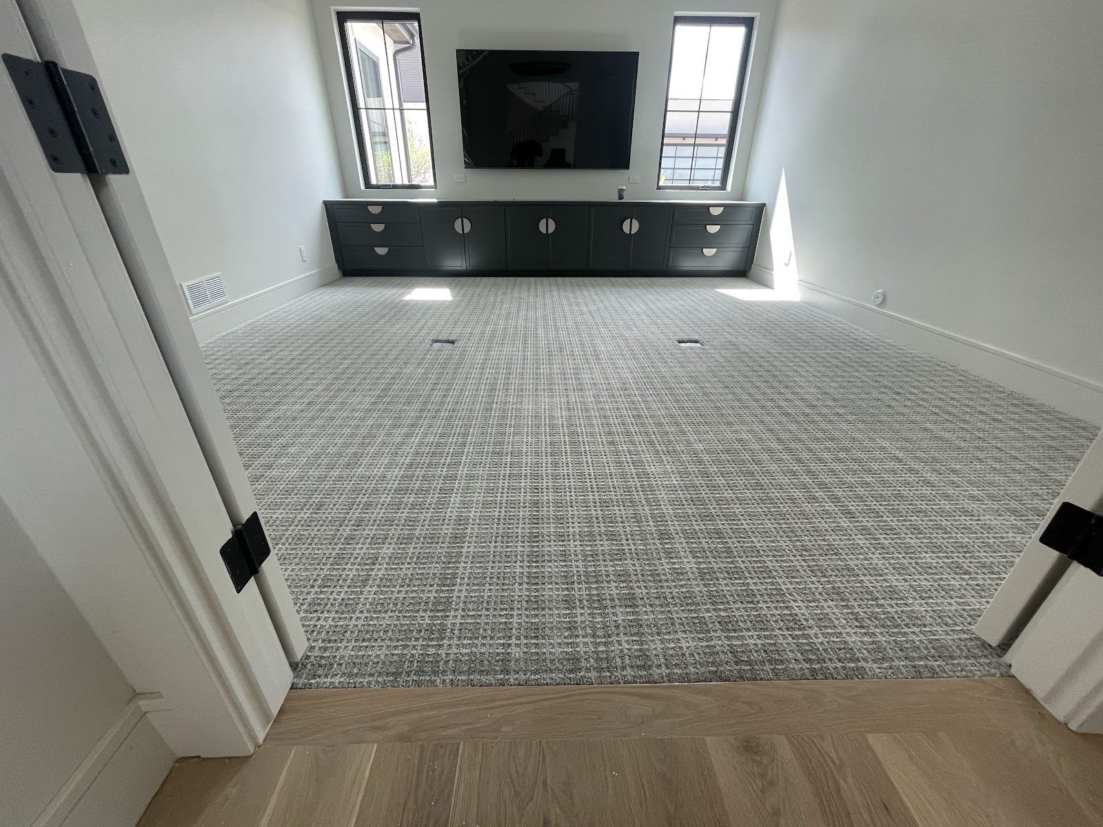 Patterned gray carpet in a room with built-in dark cabinets, meeting a hardwood floor at the doorway