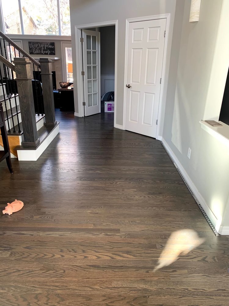 Dark-stained hardwood floor in a home entryway with a staircase and white doors
