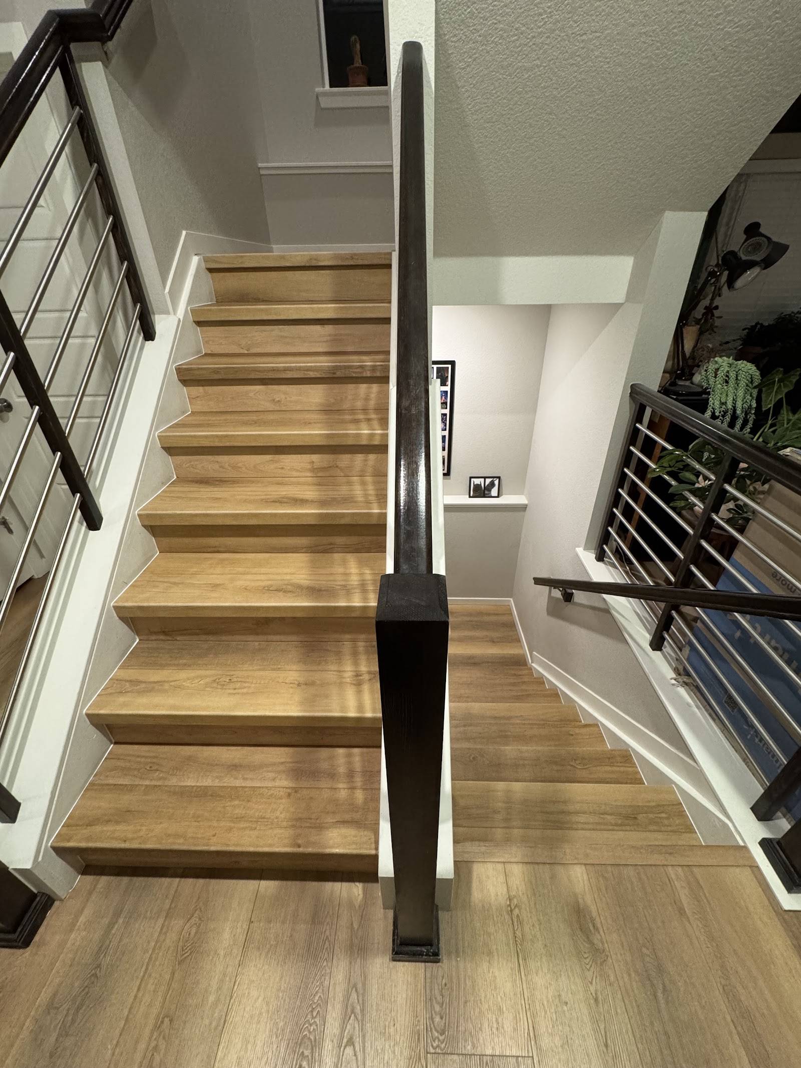 Staircase with wood-look vinyl plank treads and risers and a dark metal railing, leading down to matching flooring