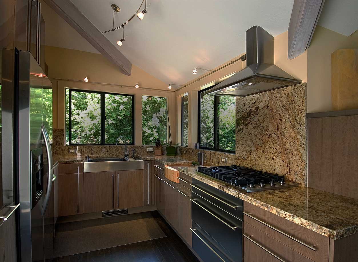 Remodeled kitchen with granite backsplash, stainless range hood, gas cooktop and wood-toned flat-panel cabinets beneath a vaulted ceiling