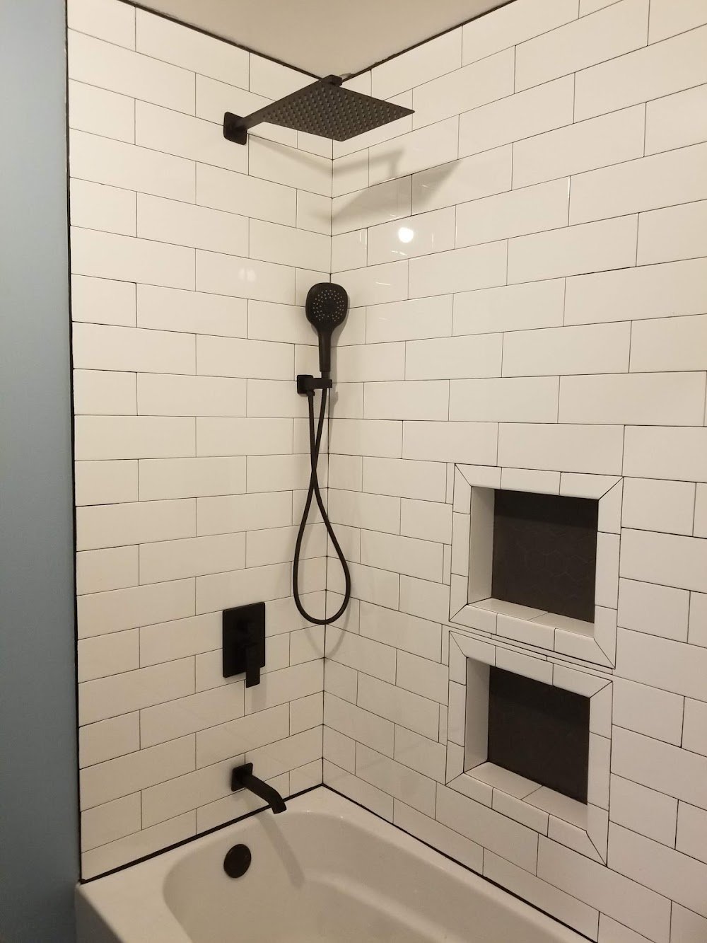Tiled bathtub shower with white subway tile, matte black fixtures and two recessed niches