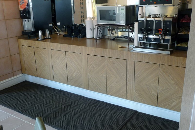 Wood-grain laminate cabinet fronts and countertop forming a coffee and beverage service counter in a restaurant