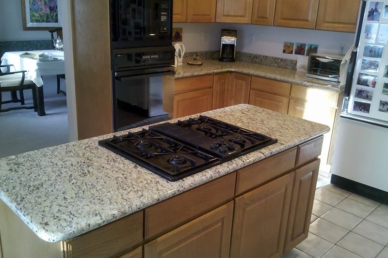 Granite-look countertop on a kitchen island with a built-in gas cooktop and oak cabinets