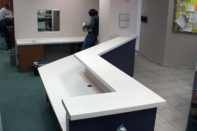 White laminate reception counter with an angled, seamless top installed in a commercial lobby while a worker stands nearby