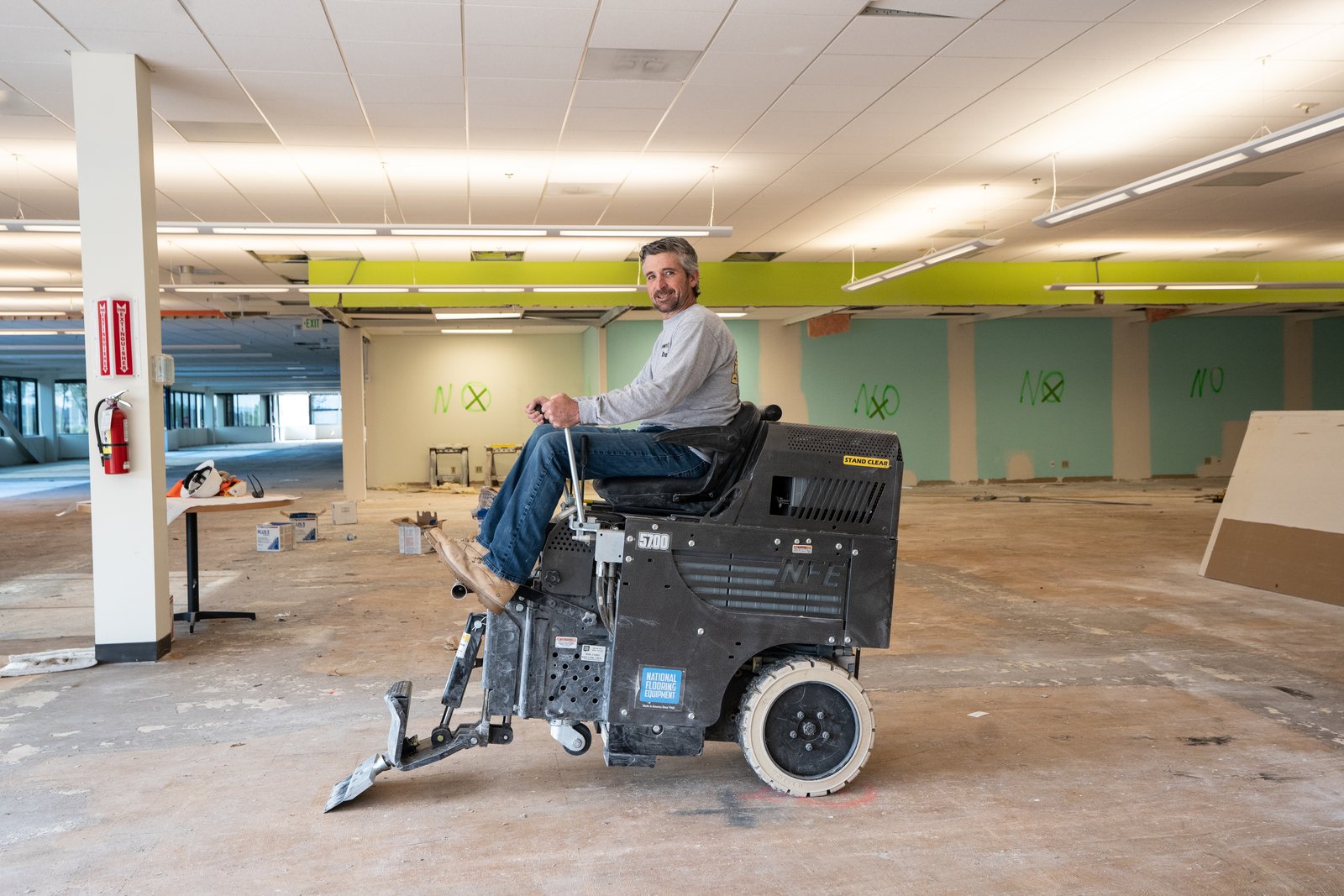 Mike Keigher sits at the controls of a ride-on floor scraper on the bare concrete floor of a gutted office