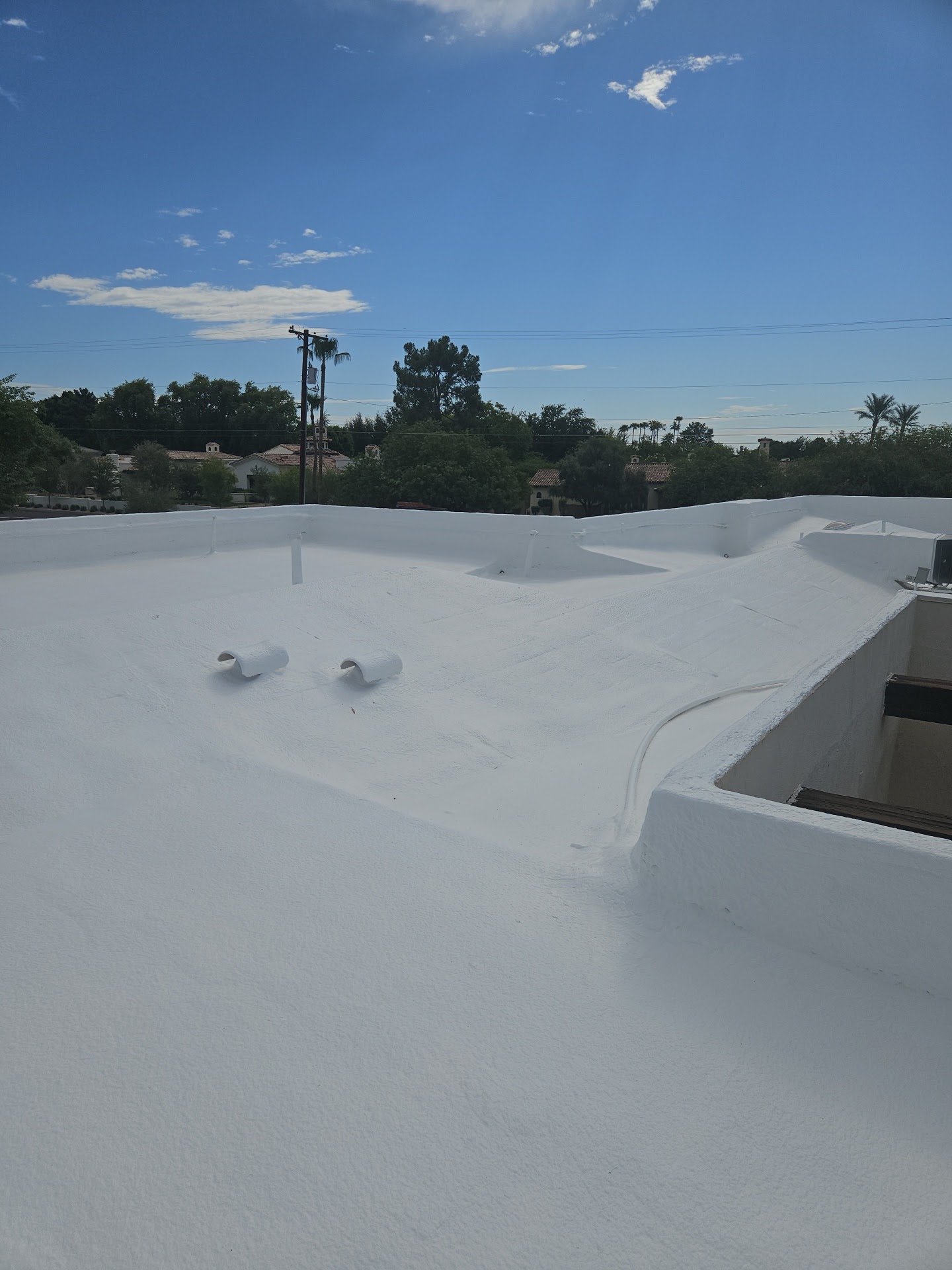 Smooth white coated foam flat roof with parapet walls and two vents under a blue sky