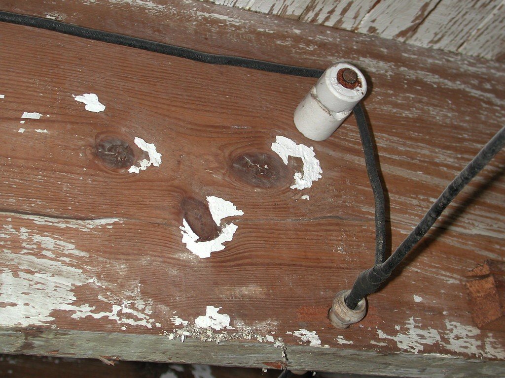 Old black knob-and-tube wire running past a white porcelain knob on a weathered wooden beam