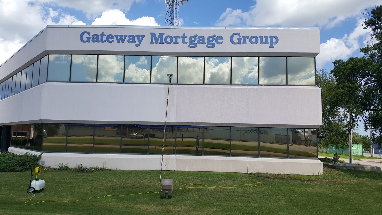 A water-fed pole leans against the glass of a two-story Gateway Mortgage Group office, with a hose cart on the lawn