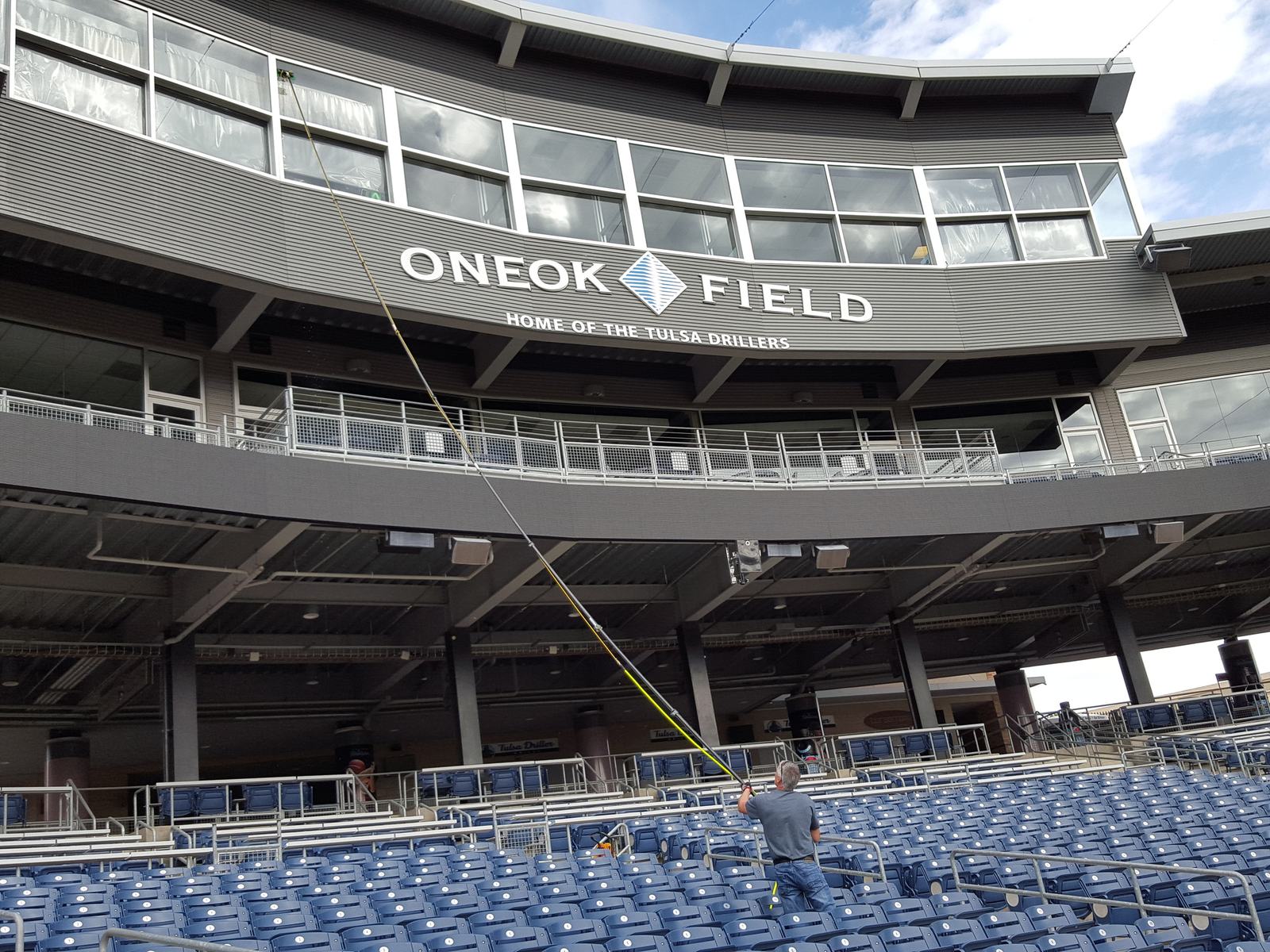 A window cleaner standing in the seats at ONEOK Field reaches a long water-fed pole up to a row of windows above the stands