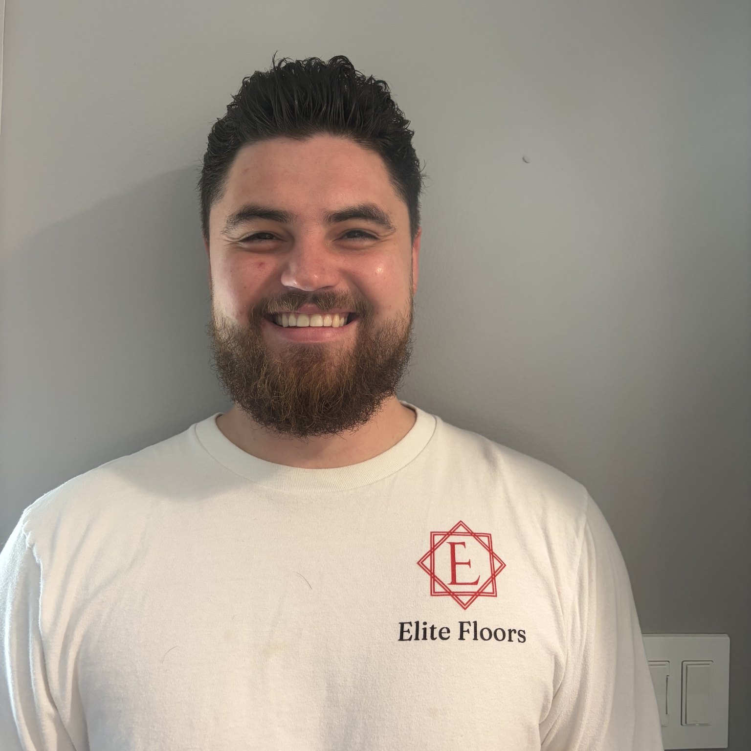 Smiling bearded man in an Elite Floors logo t-shirt, representing Elite Floors LLC