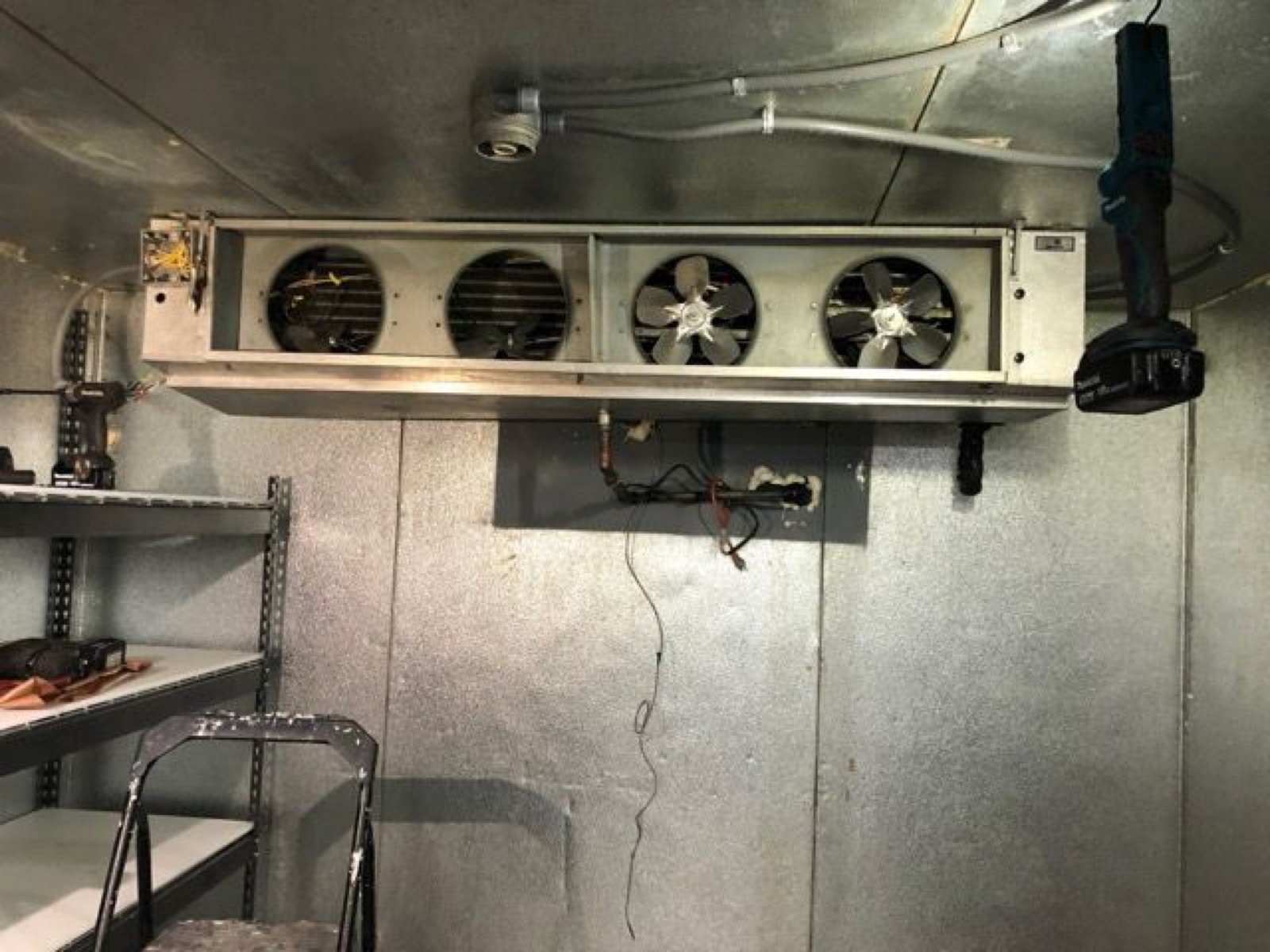 Walk-in cooler interior with an evaporator unit mounted on the ceiling, four fan openings, and a cordless drill nearby
