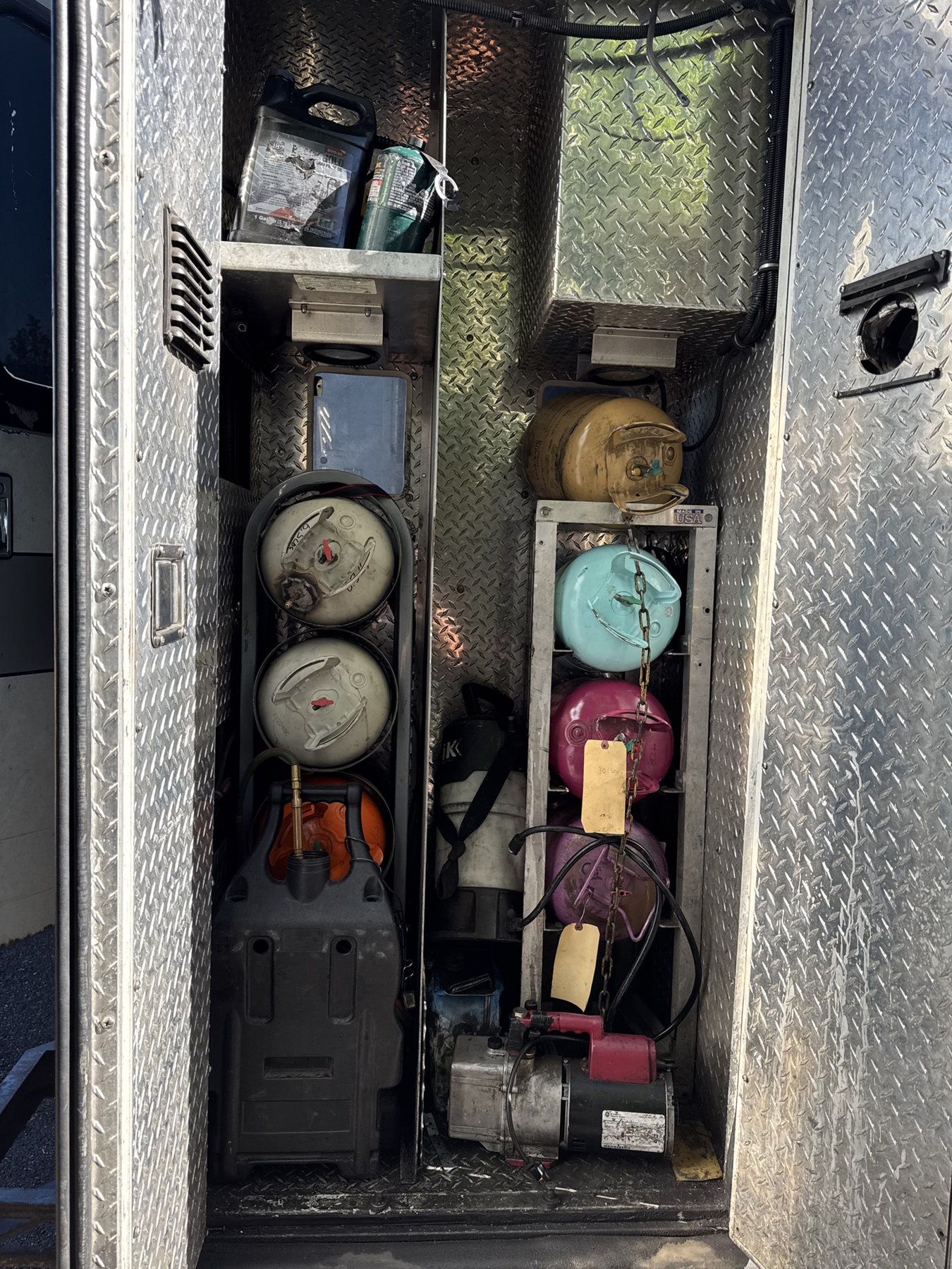 A side compartment of the service truck holding refrigerant tanks of several colors, a recovery machine and a vacuum pump