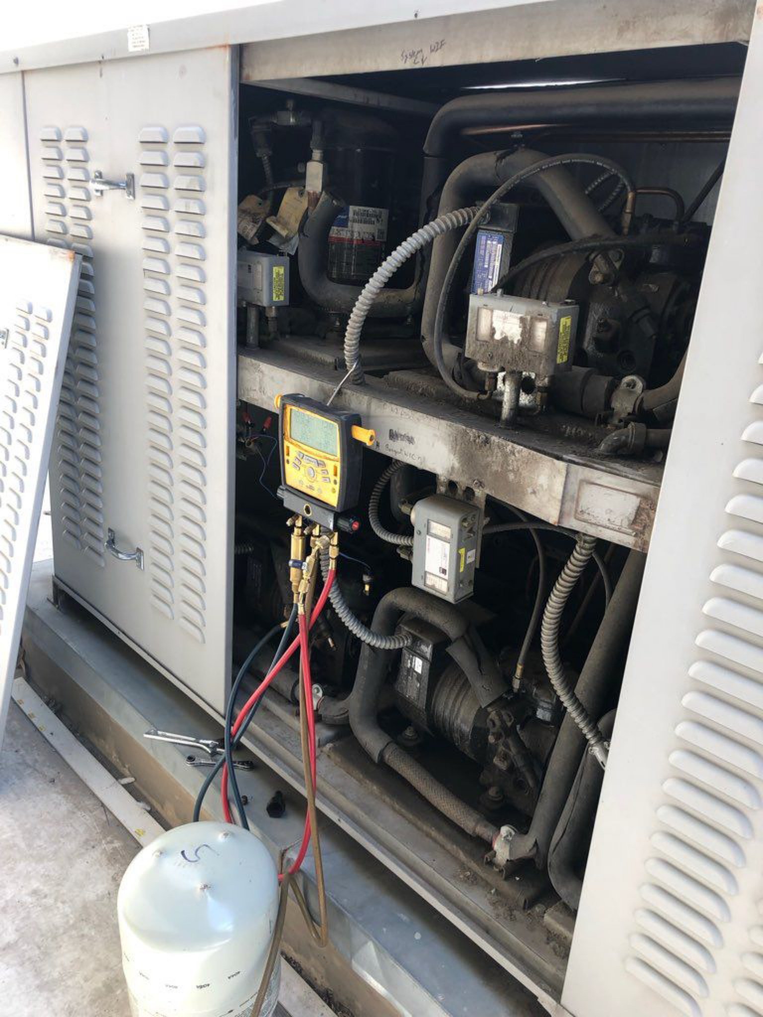 Open commercial refrigeration condensing unit with a digital manifold gauge set hooked up and a refrigerant tank beside it