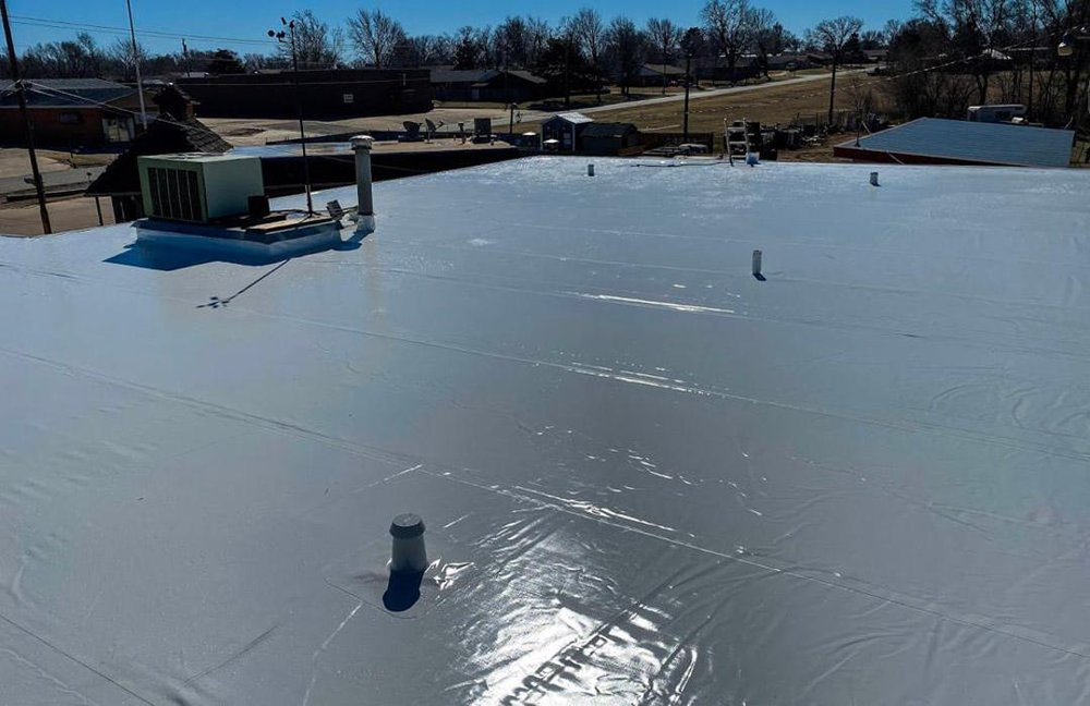 Newly installed white single-ply membrane on a flat commercial roof, with rooftop vents and an HVAC unit