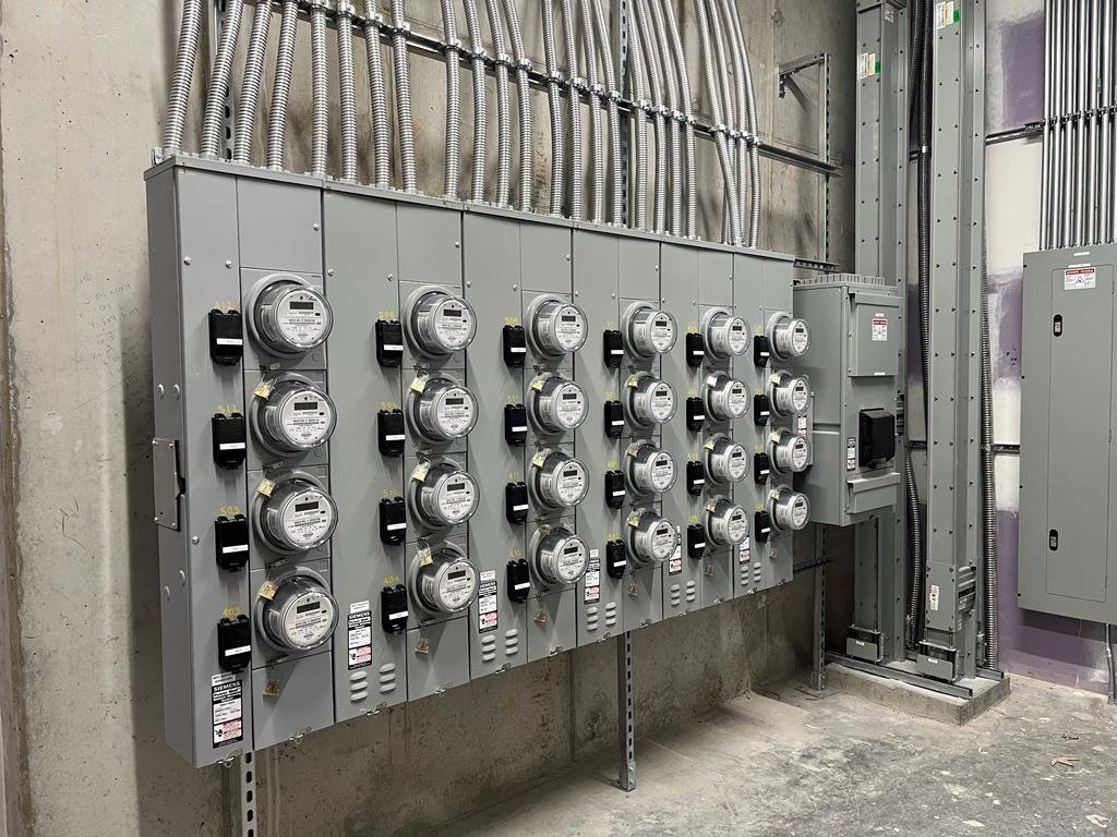 Wall of electric meters and metal conduit runs mounted in a concrete utility room