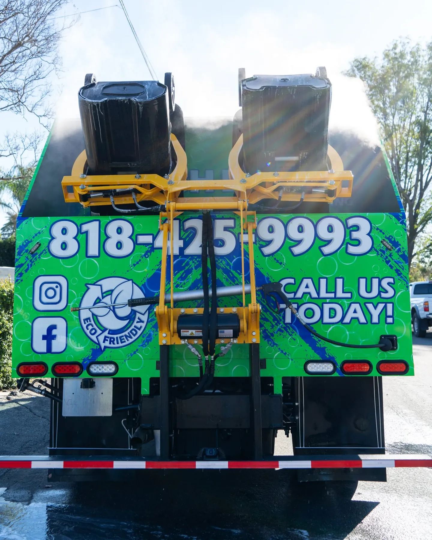Rear of the green Fresh Bins LA truck with two bins raised on the yellow lift arm