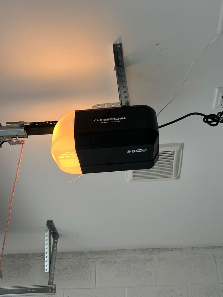 Black Chamberlain garage door opener with an illuminated light lens mounted to a garage ceiling bracket