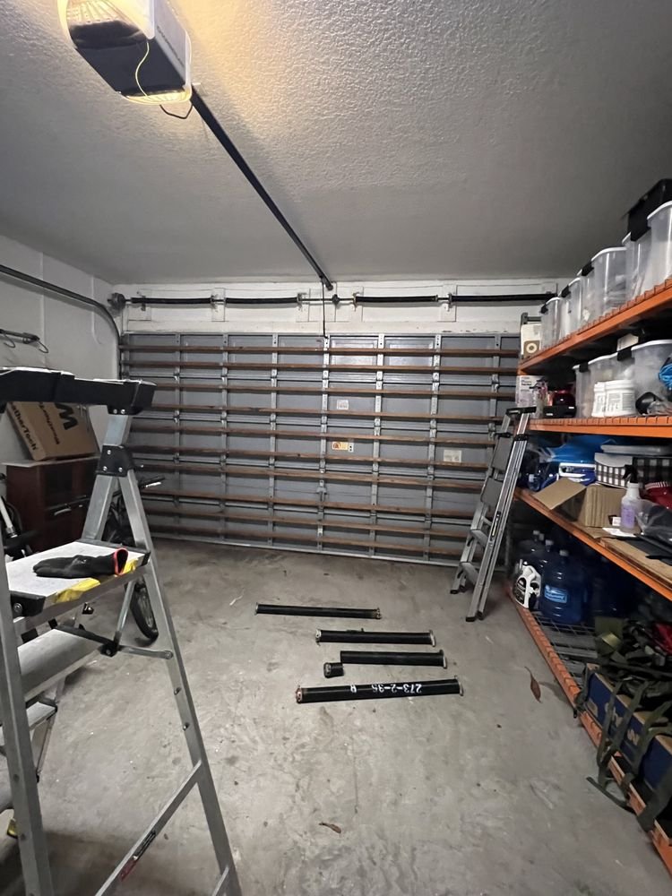 Garage interior with removed torsion spring tubes laid on the floor in front of a sectional door and a ladder