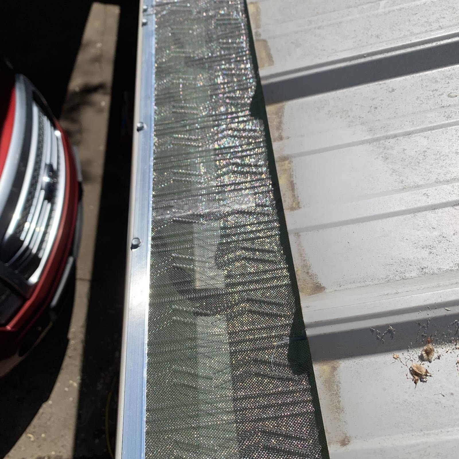 Silver micro-mesh gutter guard fitted over a gutter along the edge of a metal roof
