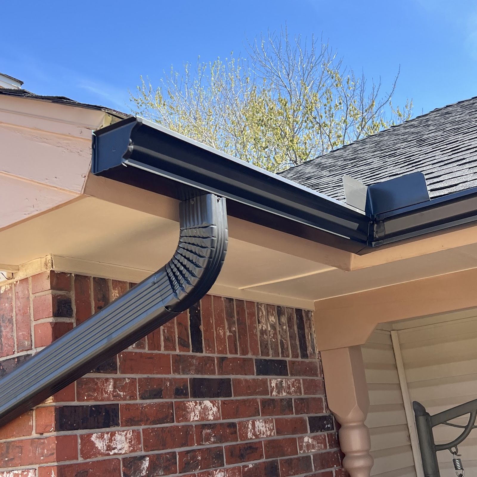 A new black gutter and downspout at the roof edge of a red-brick house