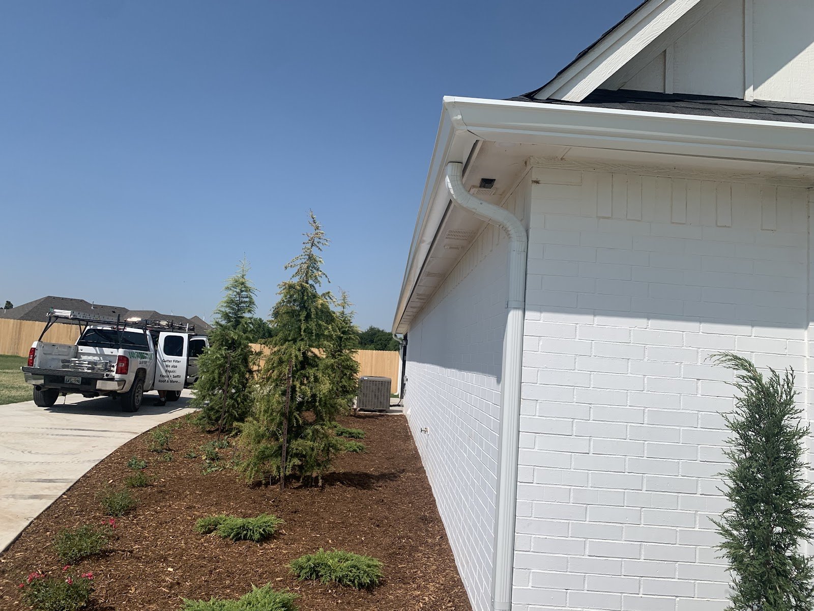 White gutter and downspout on a newly built white-brick house, with a work truck lettered "Gutter Filter" parked in the driveway