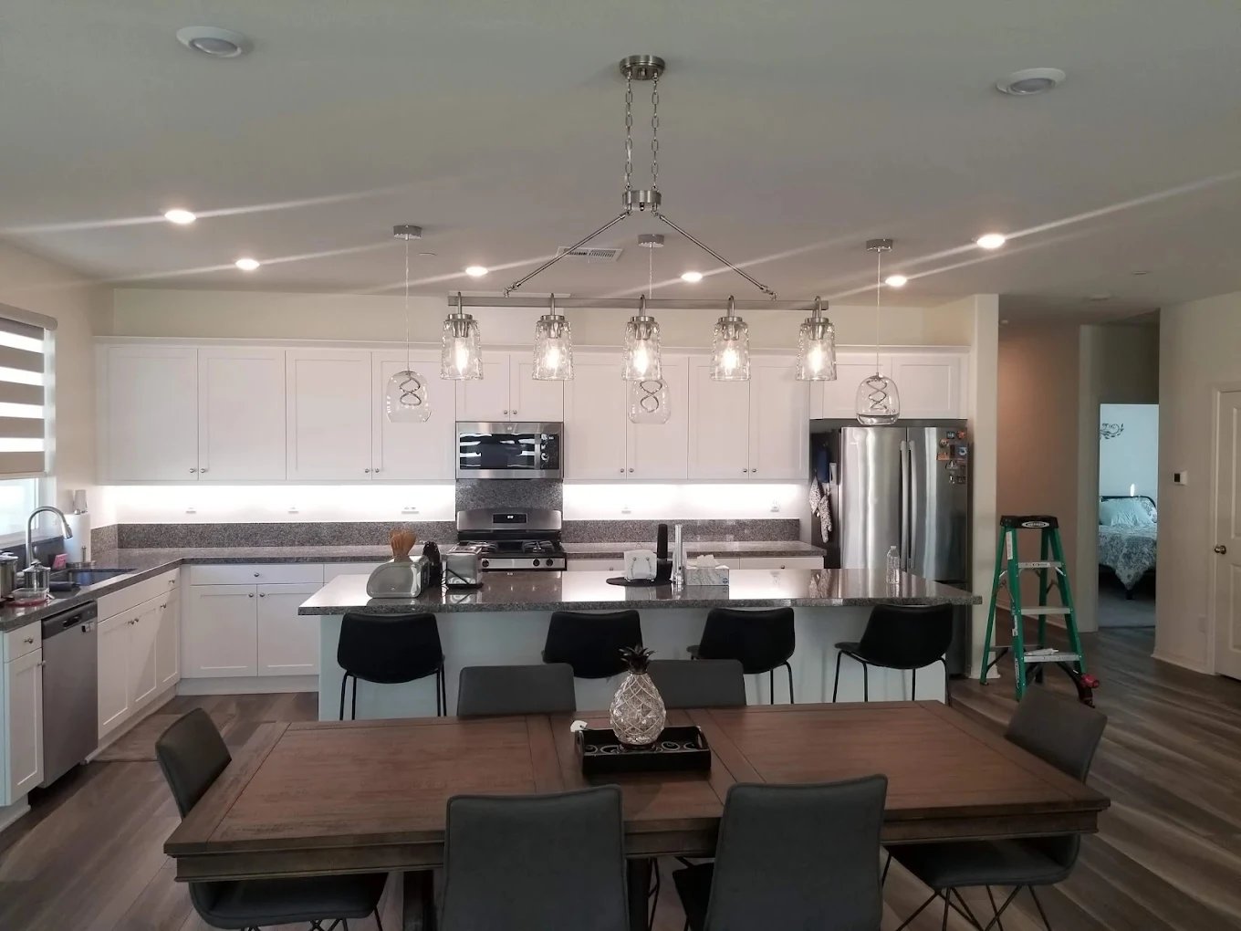 Open-plan kitchen with pendant lights over an island, recessed ceiling lights and lit under-cabinet strips, with a green ladder nearby