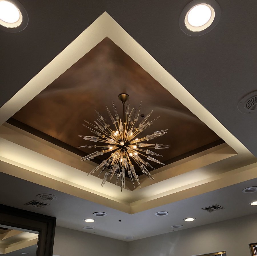 Sunburst chandelier hanging in a recessed, lit tray ceiling with copper-toned center and recessed lights around it