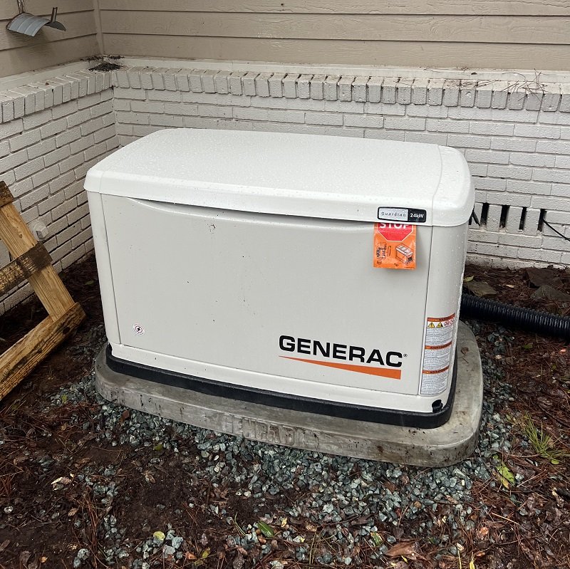 White Generac standby generator on a gravel-edged pad against a brick-faced exterior wall