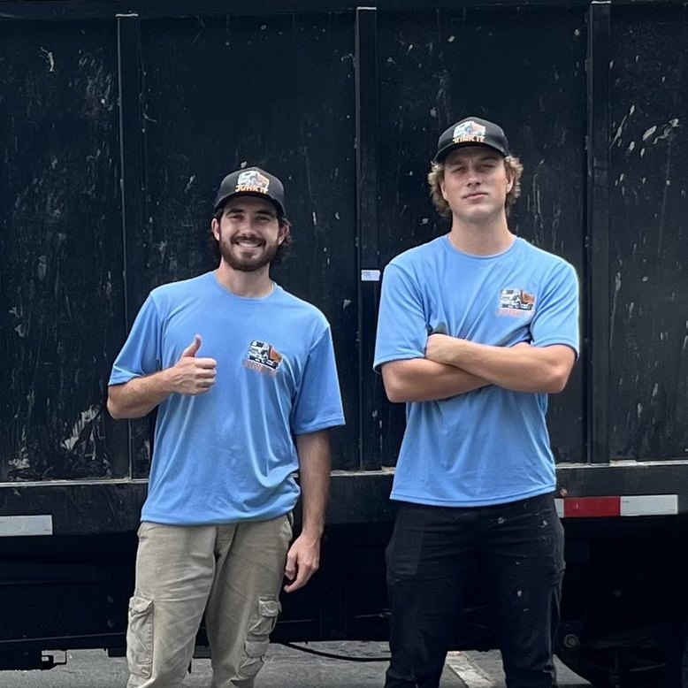 Two Junk It team members in blue shirts and caps standing in front of their dump truck