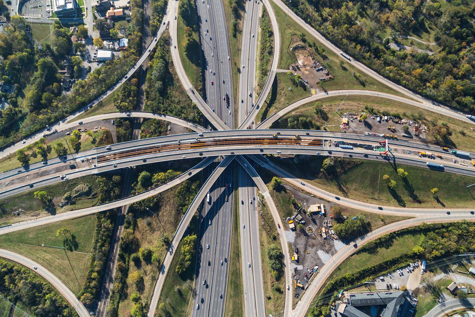 Aerial view of a multilevel highway interchange with ramps, traffic and construction staging areas among trees