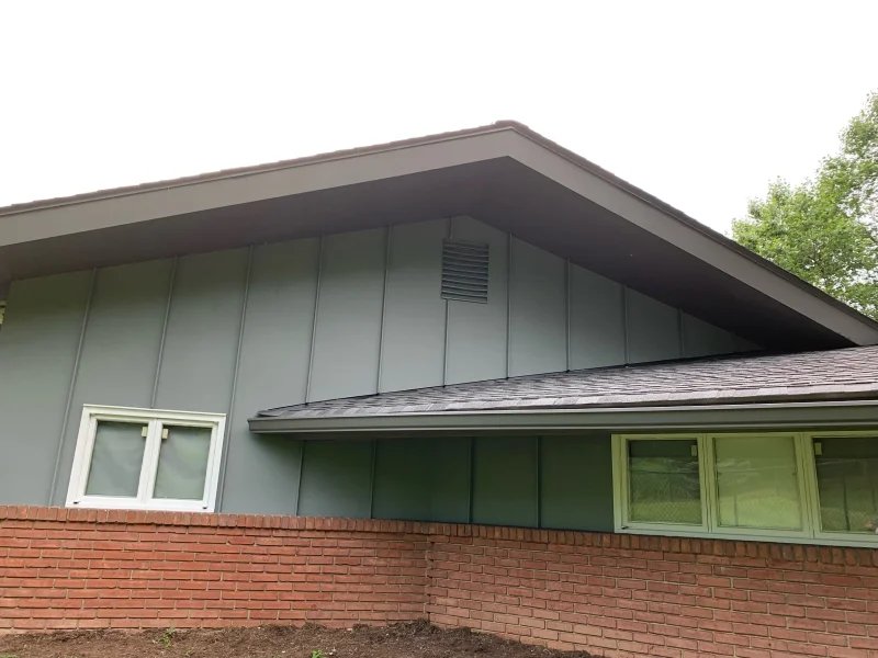 House exterior with fresh gray-green vertical siding and brown trim above a red brick wall