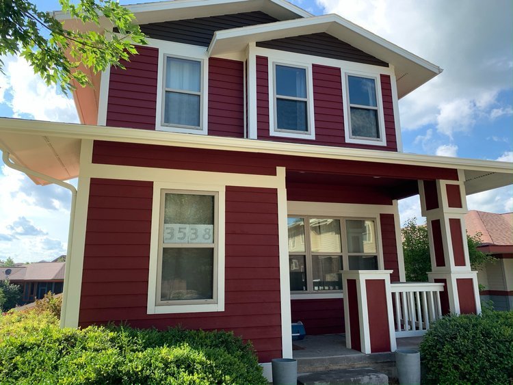 Two-story house with freshly painted deep red siding, cream trim and a front porch with white railings