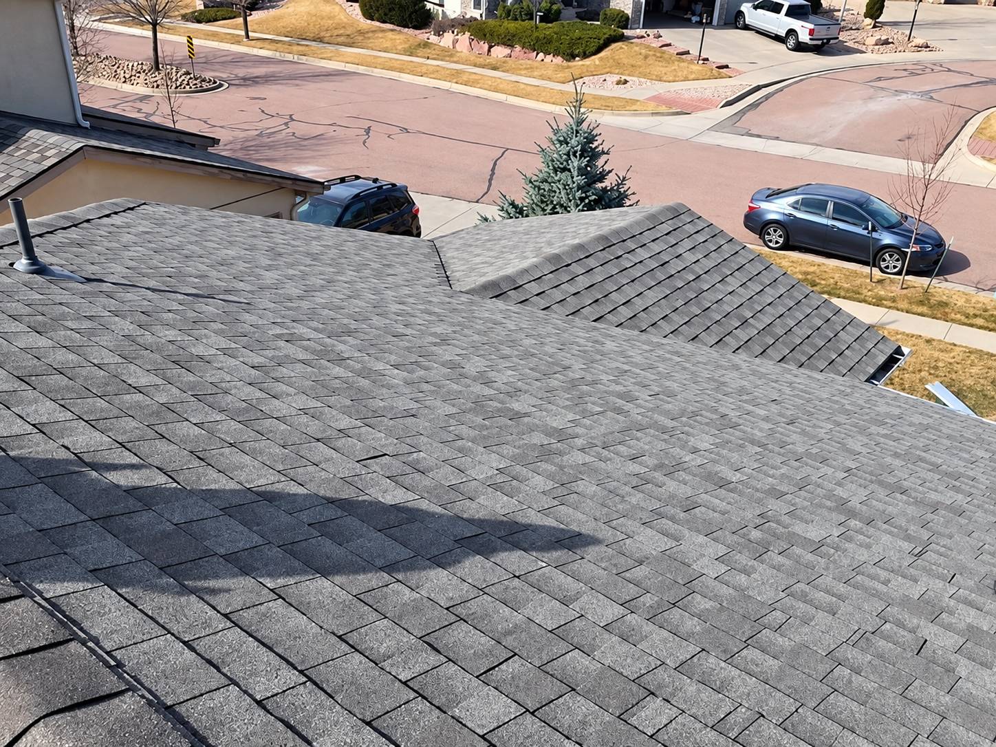 Newly shingled gray asphalt roof on a Colorado Springs home, with a residential street and parked cars below