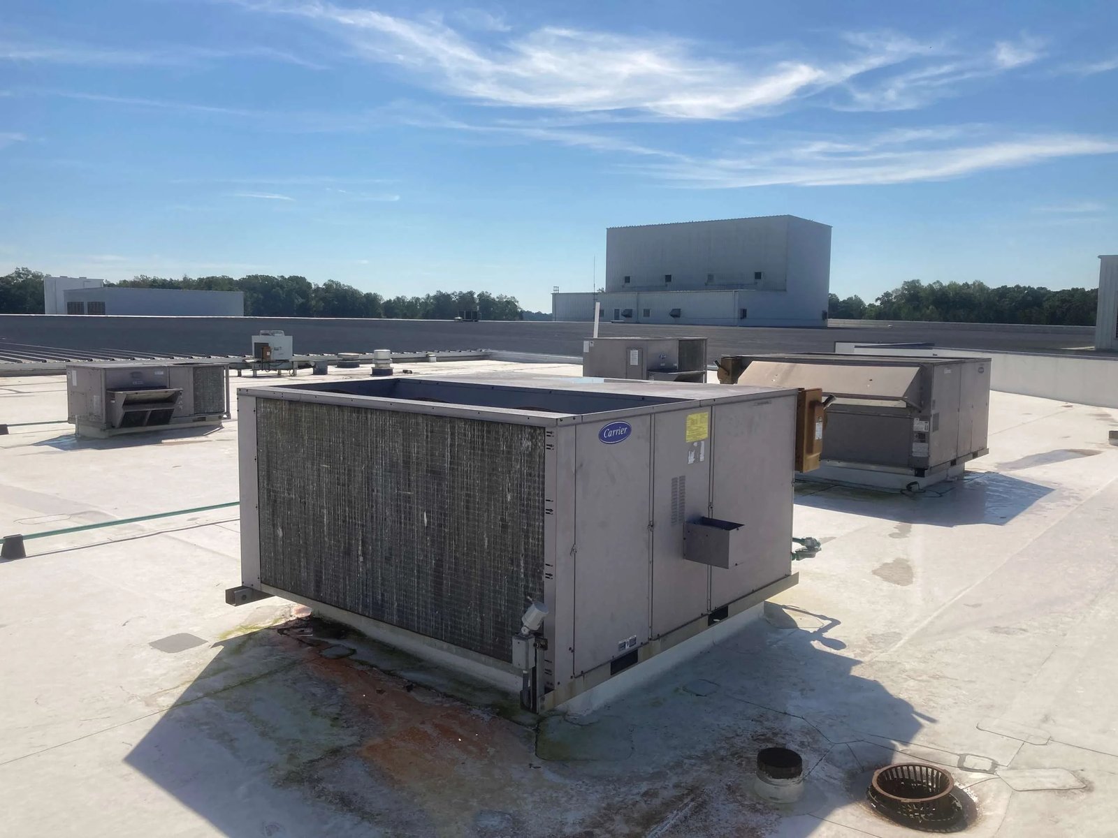Large Carrier rooftop HVAC unit on a flat commercial roof with other equipment and a blue sky behind
