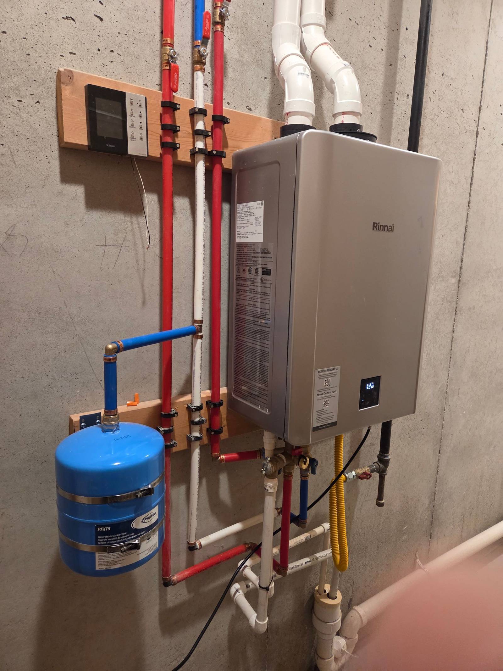 Wall-mounted Rinnai tankless water heater with PVC venting, color-coded red and blue piping and a blue expansion tank